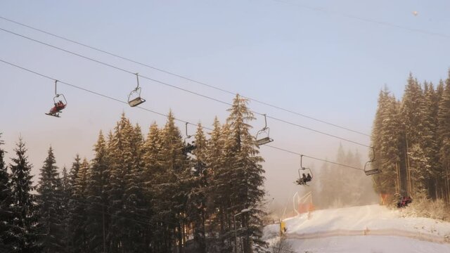 Ski lift in ski resort in motion with people during winter morning. Using chairlift at scenic background pine trees in snow, forest, sky, track for skiing. Snowy winter vacation Carpathian mountains