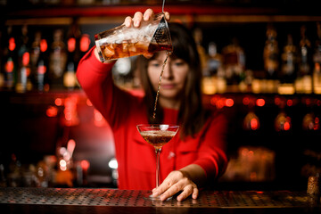 view on wineglass standing on bar and bartender holding mixing cup and accurate pours drink into it