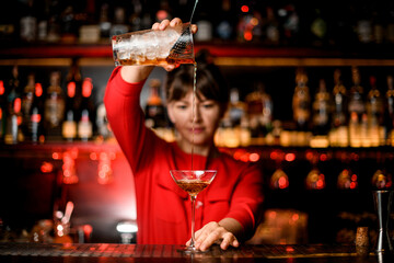 view on wineglass standing on bar and bartender holding mixing cup and skilfully pours drink into it