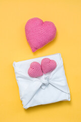 Zero waste valentine's day. Eco friendly gift furoshiki and knitted hearts on yellow background. Vertical view