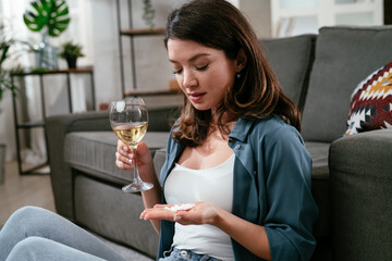Young women drinking medicine pills and wine. Sad girl sitting on the floor.
