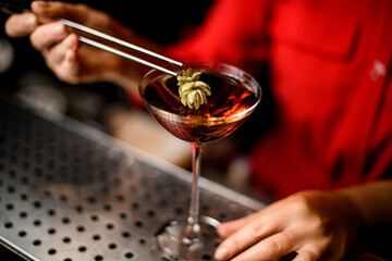 close-up view of glass with drink which female hand with tweezers decorates with green hop