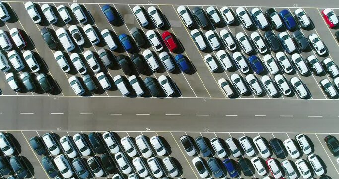 Aerial view above a large number of cars parked in a parking lot, in angled parking spaces. 4K
