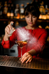martini glass with drink stands on bar counter and woman bartender accurate sprinkles on it