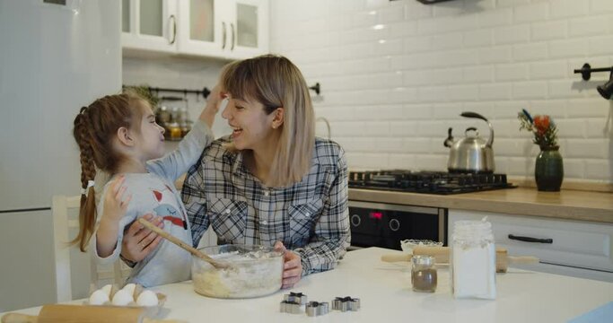 Young family spending time at home together. Mother and daughter having fun baking cooking christmas cookies pastry in the kitchen. Loving happy mom hugs and kisses her cute kid laughing