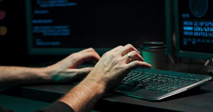 Close up on the hand of a young hacker who is typing on a computer keyboard with malware. An anonymous online scammer is looking to steal consumer data using computers.
