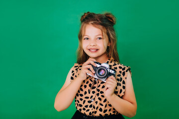 Teenage girl in colorful clothes on a green background with an adorable smile. The child holds a camera in his hands. Beginning photographer.