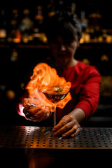 amazing view on wine glass on bar counter which female bartender accurate sprinkles and sets fire