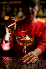 close-up view of transparent glass with drink and ice cube that woman bartender decorates