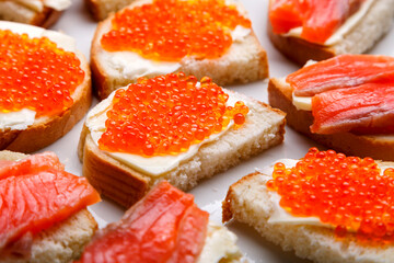 Bruschettes with butter and trout and red caviar on a white plate close-up.