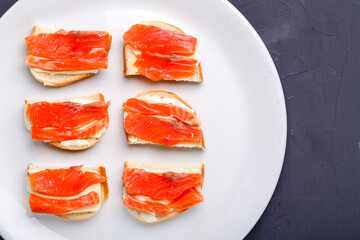 Bruschettes with butter and trout on a white plate on a gray background.