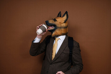 A man with a latex dog head mask and a backpack handling a smartphone, carrying a cup of coffee in...