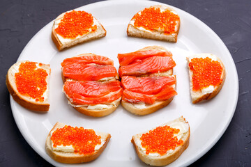 Naklejka na ściany i meble Bruschettes with butter and red caviar and trout on a white plate.
