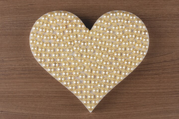 Heart with pearls on wooden background.
