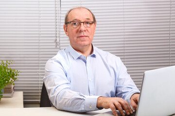 A man in the office with glasses at the computer is typing on the keyboard.