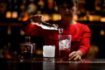 hand of woman bartender holds scoop with ice cubes and accurate pours them into glass