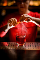 view of glass with drink on which hands of bartender sprinkles juice of zest