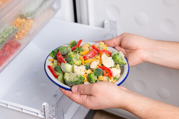 A person is taking a plate of frozen vegetables out of the freezer of the fridge. Concept of frozen...