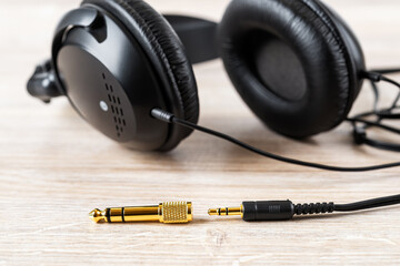 Fototapeta na wymiar Golden TRS adapter and jack near black wired over ear headphones on a desk. Gold plated plugs for high quality audio. Modern personal gadget for listening to music.