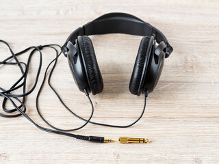 Black wired over ear headphones nead golden TRS adapter and jack on a desk. Gold plated plugs for high quality audio. Modern personal gadget for listening to music.