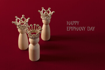 Three wise men figures with crowns on red background and the text Happy Epiphany day. Copy space.