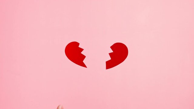 Hands tear apart the shape of a red heart on pink background. Broken heart, divorce and separation concept. No love, break up. Heart problems.