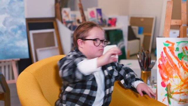 A boys plays a stone, scissors, paper game at art workshop. The camera is shaking in the hands of a classmate who is filming a video. Communication with individuals with Down Syndrome in classroom.
