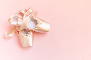 New pastel beige ballet shoes with satin ribbon isolated on pink background. Ballerina classical...