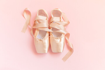 New pastel beige ballet shoes with satin ribbon isolated on pink background. Ballerina classical pointe shoes for dance training. Ballet school concept. Top view flat lay, copy space