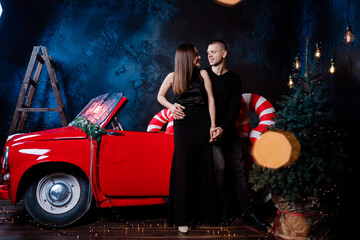 Fototapeta na wymiar Young happy couple man and woman in love in Christmas are hugging near a red retro car with New Year's gifts. Kiss, girl, happiness, quarantine Christmas celebration, holiday.