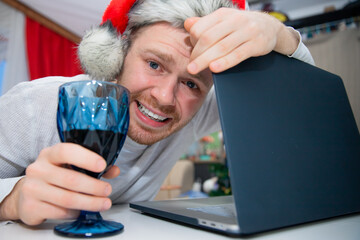 Young happy man having video call via laptop with wine, celebrating Christmas alone at home