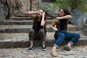 Two women fighting and pulling each others hair while sitting on a stoned  ladder.
