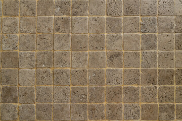 Mosaic texture made of natural sandstone. Closeup on a small square stone pavement background.