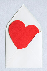 Top view of an open envelope with red felt heart on a white felt background. The concept of Valentine's Day