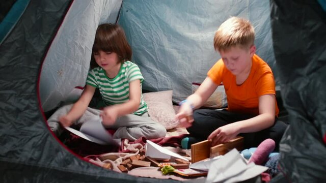 Children spend time in a tent in the evening. The boy adds cubes. He makes a craft out of paper with his hands. Intellectual games of children in self-isolation.