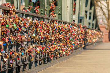Obraz premium Many locks on the green bridge railing of the iron bridge in Frankfurt over the river Main. Locks of love in different colors in sunshine with blurry background