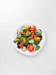 White plate with a bright fresh vegetable salad of vegetables and greens on a light background