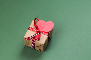 Gift box with bow and paper heart on a green background. Valentine's Day.