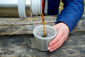 Fototapeta na wymiar a man's hand holds a mug into which tea is poured from a thermos