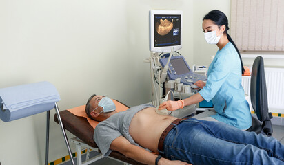 A young girl doctor makes an examination of the abdominal cavity on an ultrasound machine in a male patient.