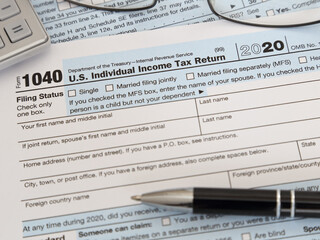 An IRS 1040 tax year 2020 form is shown in 2021, along with an ink pen, calculator, and glasses. The Internal Revenue Service tax filing deadline is currently scheduled for April 15 this year.