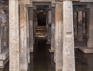 Hampi, Karnataka, India - November 4, 2013: Prasanna Virupaksha underground Shiva Temple. brown stone pillars standing in submerged water. Inner sanctum at end.