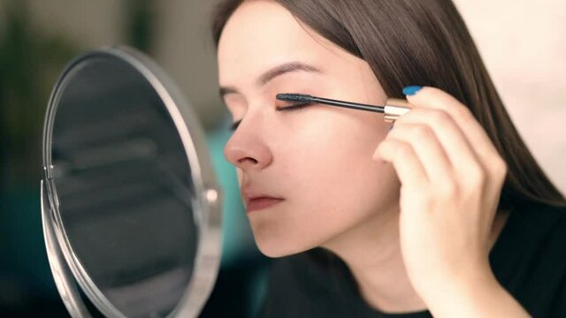 Young woman putting on makeup while looking in the mirror paints eyelashes mascara for the eyes