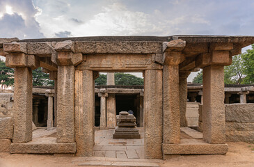 Fototapeta premium Hampi, Karnataka, India - November 4, 2013: Prasanna Virupaksha underground Shiva Temple. Brown stone ruins in front of lower lying sanctum under sunset cloudscape.