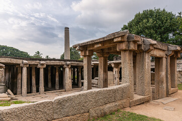 Fototapeta premium Hampi, Karnataka, India - November 4, 2013: Prasanna Virupaksha underground Shiva Temple. Brown stone ruins around under sunset cloudscape with green foliage.