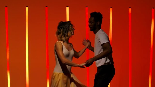 A beautiful sensual couple perform passionate dance steps of Hispanics against a bright red orange neon background. A man and a woman are dancing salsa in slow motion. Close up.