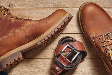 Leather men's boots and belt on wooden background. Fashion trend of casual style. Top view.