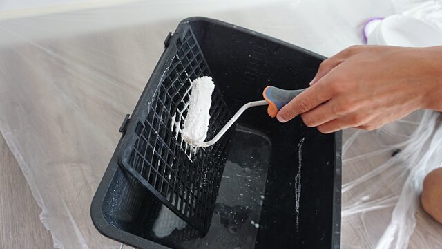 Mano escurriendo rodillo con pintura blanca