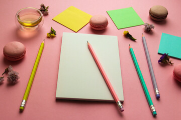 Creative feminine workspace with sketchbook for drawing, pencils, a cup of tea and macaroons on pink background. Art concept