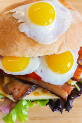 Closeup shot of mouthwatering sandwich, made of three fried quail eggs, and other stuffing including vegetables, taken from above